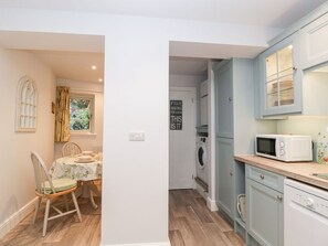 A compact kitchen with a microwave, dishwasher, and a dining area with a table and chairs. - The Old Thatch, Porlock. 1bed. (Minehead)