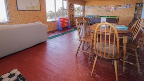 A room with a wooden ceiling, a white couch, a dining table with chairs, a pool table, and a dartboard. - Cabin 8 Inis Dumhaigh (Gortahork)