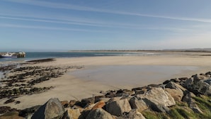 A coastal landscape with a sandy beach, rocky shoreline, and a distant view of a boat and land. - Cabin 9 Inis Beag (Gortahork)