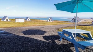 A gravel path leading to a row of small, white cottages with blue roofs, a picnic table, and a blue umbrella. - Cabin 10 Inis Bo Finne (Gortahork)