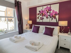 Une chambre d’hôtel avec un lit, deux tables de chevet, une fenêtre avec des rideaux, un mur orné d’un tableau floral et une vue sur l’extérieur.