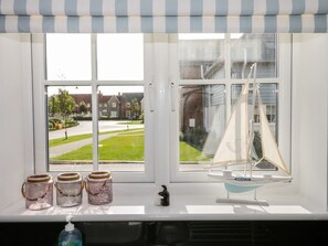 Una ventana con vistas a una zona residencial, un modelo de velero y tres frascos en el alféizar.