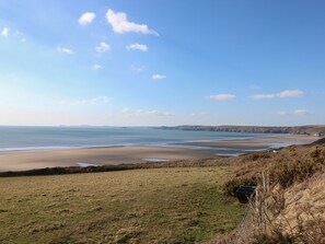 A coastal landscape with a grassy field, a sandy beach, and a clear sky. - Coach House, near Broad Haven. (Haverfordwest)