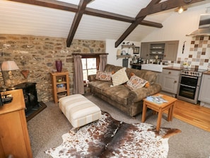 A cozy living room with a stone wall, a brown sofa, a wooden coffee table, a leather rug, and a kitchen in the background. - Coach House, near Broad Haven. (Haverfordwest)