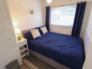 Een slaapkamer met een bed, nachtkastje, lamp, raam met gordijnen en een wandlamp.
