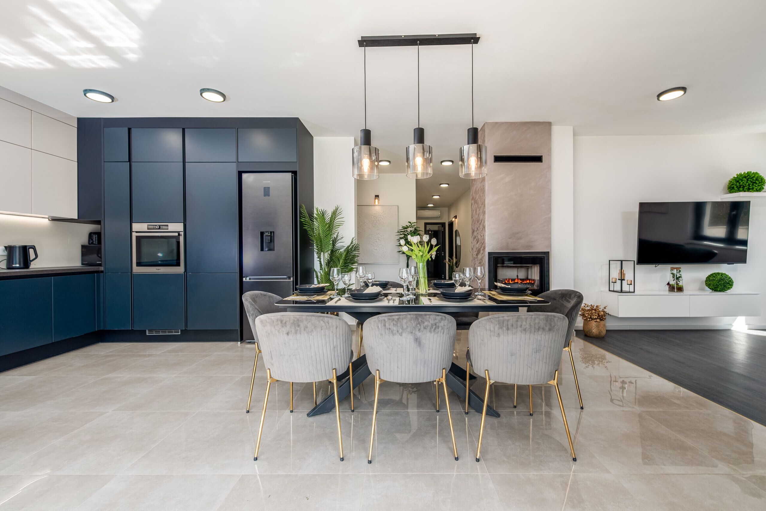 A modern kitchen with dark blue cabinets, a stainless steel refrigerator, and a dining area with a glass table and four chairs.