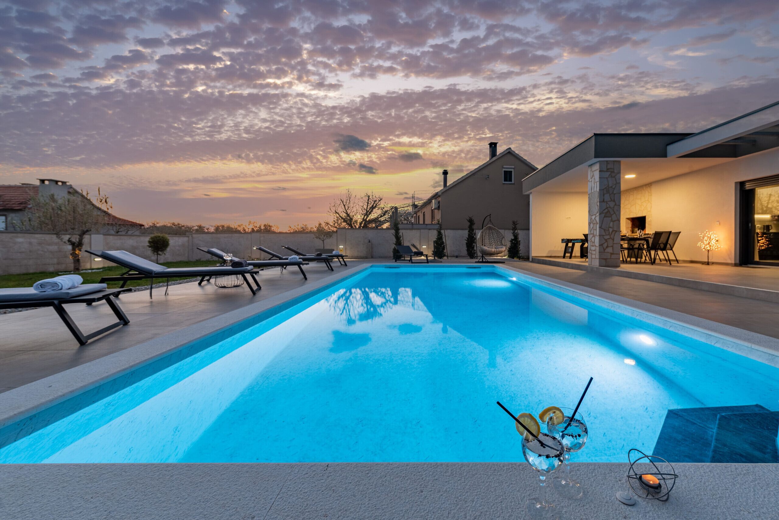Una piscina amb gandules, un piló de pedra i una zona de menjador amb cadires i taula.