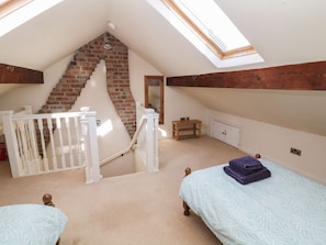 A bedroom with a sloped ceiling, a brick staircase, a white railing, a bed, and a small wooden table.