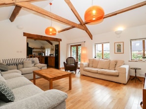 A spacious living room with a wooden floor, a sofa set, a coffee table, and pendant lighting.