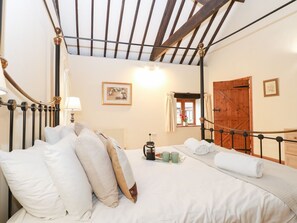 A bedroom with a bed, pillows, a bedside table with a lamp, a window, and a wooden door. - Pear Tree, Wood Norton (Dereham)