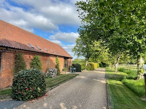 A brick building with a gravel driveway, a hedge with red flowers, and a large tree providing shade. - Pear Tree, Wood Norton (Dereham)
