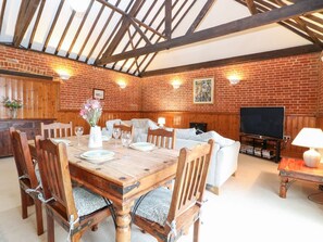 A dining area with a wooden table and chairs, a sofa, a TV, and a fireplace. - Pear Tree, Wood Norton (Dereham)