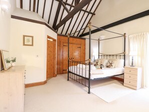 A bedroom with a four-poster bed, wooden wardrobe, and a small bedside table. - Pear Tree, Wood Norton (Dereham)