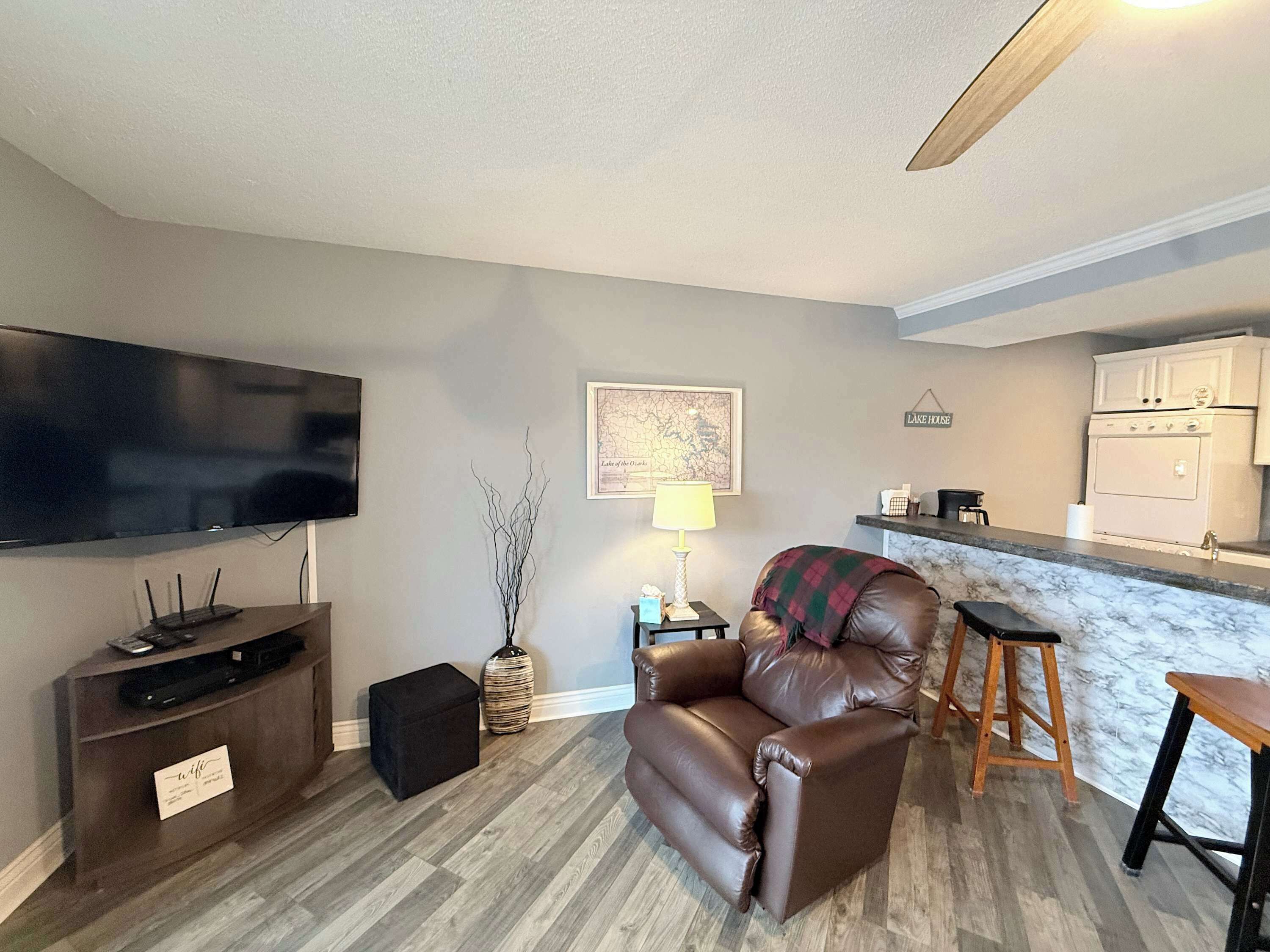 Sala de estar con televisor de pantalla plana, chimenea, sofá y zona de cocina con mostrador y armarios.