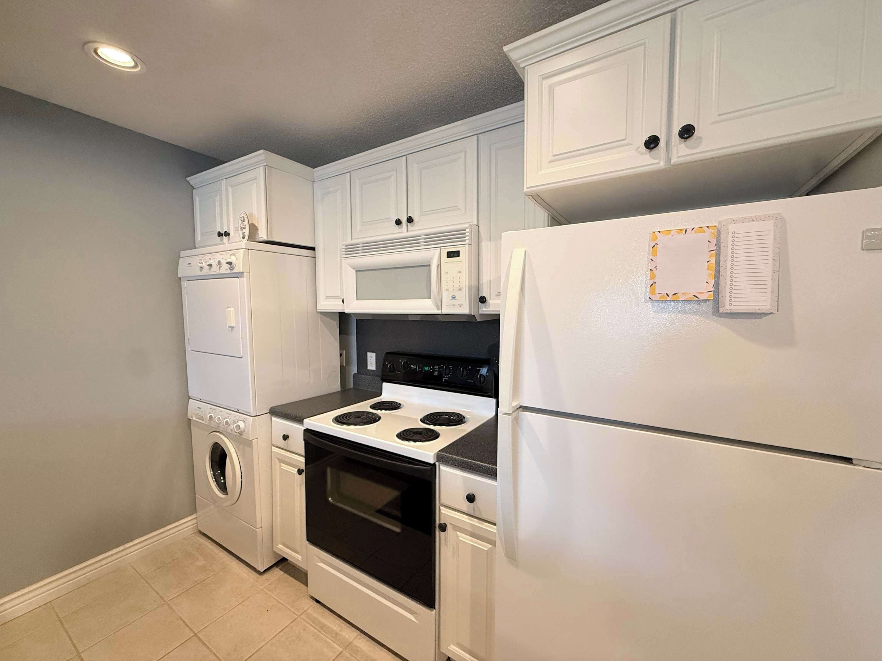 A kitchen with white cabinets, a microwave, a stove, a refrigerator, and a washing machine.