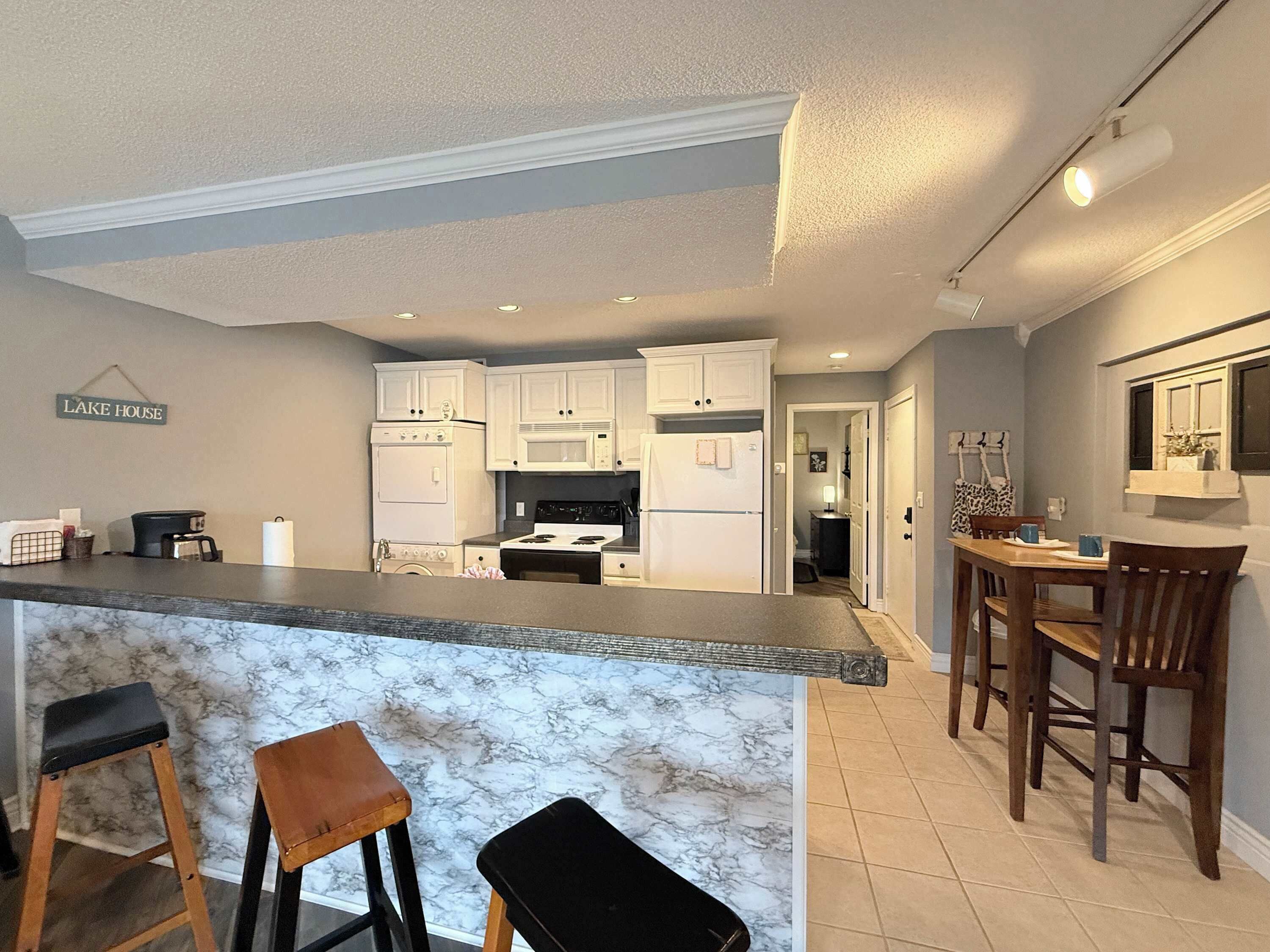 A kitchen with white cabinets, a marble countertop, and a bar area with stools.
