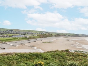 A coastal landscape with a beach, a pier, and a town in the background.