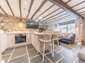 A kitchen with a stone wall, wooden beams, a built-in oven, and a bar area with two stools. - Old Toffee Shop, Ambleside (Ambleside)