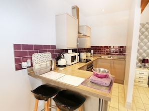 A compact kitchen with a microwave, toaster, and kettle, a small sink, and a bar area with stools. - Jack's Corner, King's Lynn (King's Lynn)