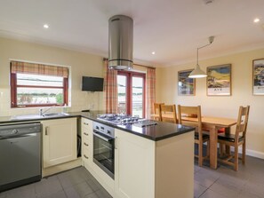Een keuken met een vaatwasser, kookplaat, oven en een eethoek met stoelen en een tafel.
