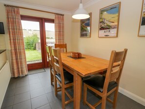 A dining area with a wooden table and chairs, a hanging light fixture, and a view through a glass door to the outside. - The Stables at Daldorch, Tarbolton (Mauchline)
