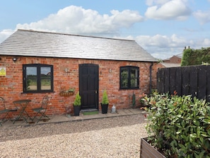 A brick building with a black door and windows, a gravel driveway, and outdoor seating.