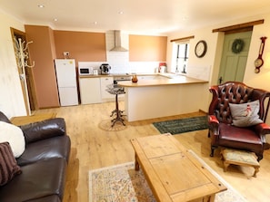 A compact living space with a kitchen, a dining area, a leather sofa, a wooden coffee table, and a red leather armchair.
