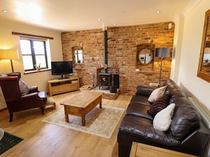 Una sala de estar acogedora con chimenea de ladrillo, sofá de cuero, mesa de centro de madera y televisor.