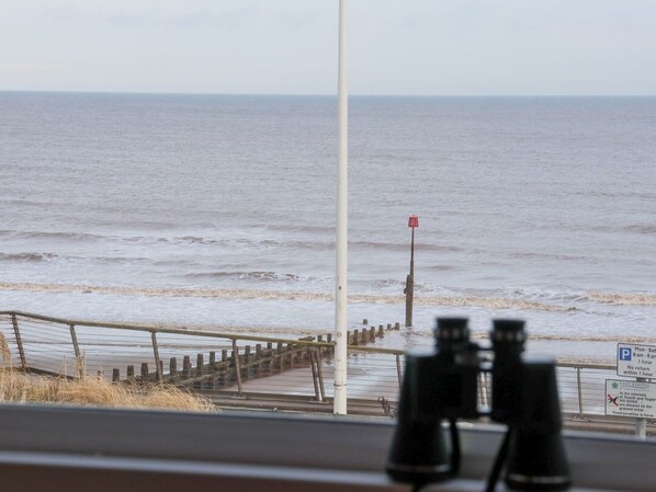 Blick aufs Meer durch ein Fernglas, ein hölzerner Steg und eine rote Boje.