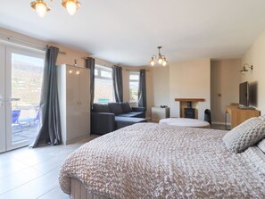 A bedroom with a large bed, a sofa, a TV, and a sliding door to a balcony. - The Willows Denbighshire 4-bed (Llangollen)