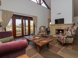 A spacious living room with a fireplace, a large window, and a television mounted on the wall.