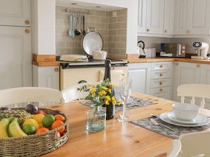 A kitchen with white cabinets, a wooden countertop, and a dining table set with a fruit bowl, a vase with flowers, and a bottle of champagne.