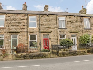 A row of stone terraced houses with a red door, a black metal fence, and a clear sky.