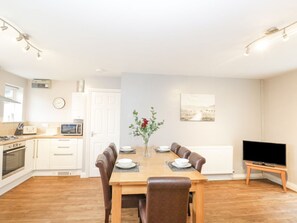 A dining area with a wooden table, chairs, a vase with flowers, a clock, and a television on a stand. - The Brambles Monmouth. Hot tub (Monmouth)