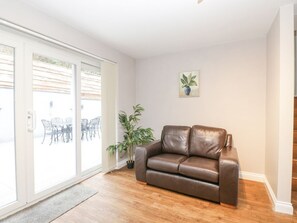Ein Zimmer mit einem braunen Ledersofa, einem Blumentopf und einer Glastür, die zu einem Außenbereich mit Tisch und Stühlen führt.