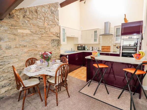 A kitchen with a stone wall, wooden dining table, chairs, and a bar area with stools.