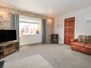 A living room with a stone wall, a wooden door, a leather armchair, a brown sofa, and a flat-screen TV on a wooden stand. - The Linhay, Chardstock, Devon (Axminster)