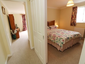 A bedroom with a bed, a nightstand, a lamp, a window with curtains, and a door leading to another room. - Charming Westmount in Ryde, Isle of Wight (Ryde)