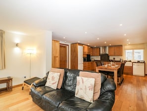 A living room with a black leather couch, wooden dining table, and kitchen in the background.