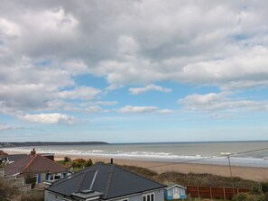 Blick auf die Küste mit Häusern, einem Strand und einem bewölkten Himmel.