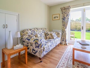 A room with a floral-patterned sofa, a wooden table, a lamp, and a radiator. - Questant Lodge, Sidmouth, Devon. (Sidmouth)