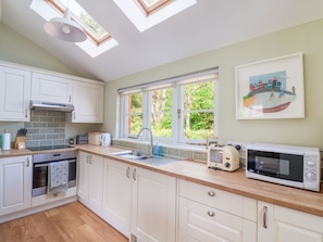 A kitchen with white cabinets, a wooden countertop, a microwave, a toaster, and a window with a view of greenery. - Questant Lodge, Sidmouth, Devon. (Sidmouth)