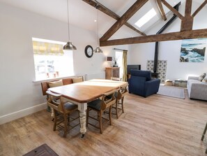 A spacious room with a wooden dining table, chairs, a sofa, a television, and a painting on the wall. - The Granary: A Luxurious Retreat in Valley (Holyhead)