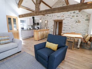 A spacious living area with a sofa, a blue armchair, a wooden dining table, and a kitchen in the background. - The Granary: A Luxurious Retreat in Valley (Holyhead)