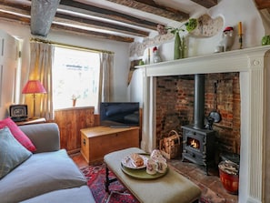 Ein gemütliches Wohnzimmer mit Kamin, einer Couch, einem Fernseher und einem Esstisch, gedeckt mit Tee und Gebäck.