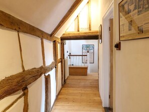 Ein schmaler Korridor mit freiliegenden Holzbalken, einer hölzernen Sitzbank und einem gerahmten Bild an der Wand.