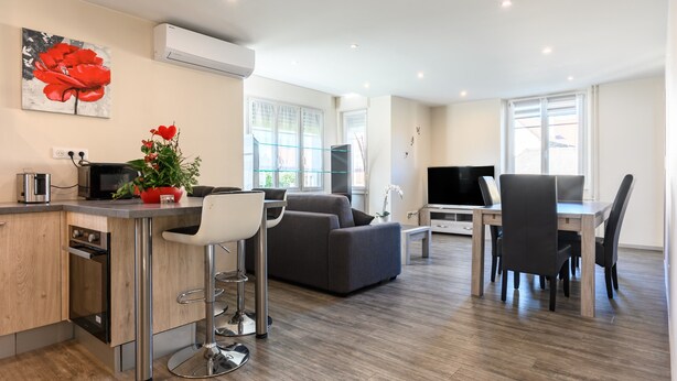 Een moderne keuken met een inbouwoven, een eethoek met tafel en stoelen, een bank en een televisie.