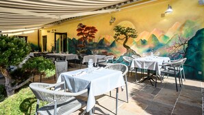 Een terras met tafels en stoelen, een muurschildering op de muur en een overdekte patio.