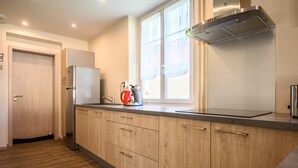Een moderne keuken met houten kastjes, een roestvrijstalen koelkast en een raam met dunne gordijnen.