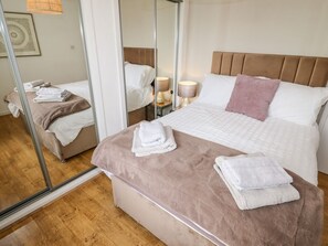 A hotel room with a bed, bedside tables, a mirror, and a wooden floor. - The Flat At Brwyn, Brynford (BRYNFORD)